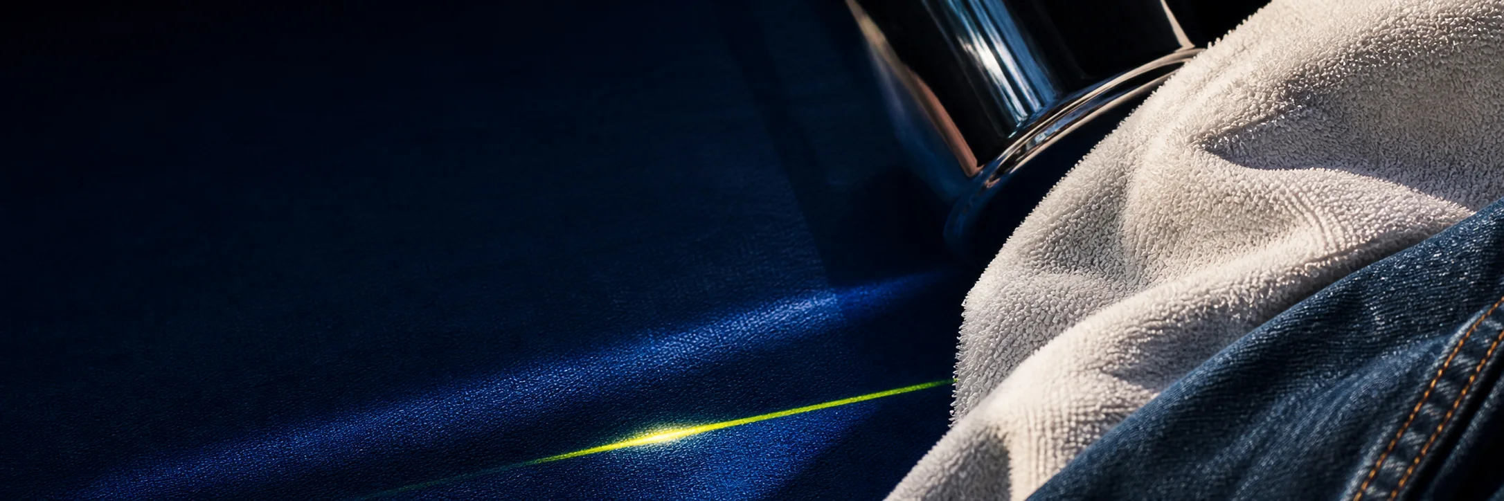 Chrome bottle and towel on deep navy fabric with a thin yellow-green light streak.
